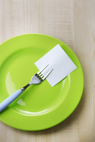 Empty note paper attached to fork, on plate, on color wooden background — Stock Photo, Image