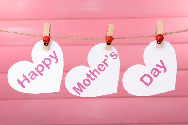Happy Mothers Day message written on paper hearts on pink background