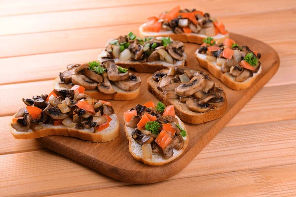 Delicious bruschetta with mushrooms on cutting board on table close-up — Stock Photo, Image