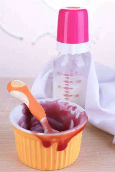 Garrafa de bebê com leite e tigela suja na mesa no fundo claro — Fotografia de Stock