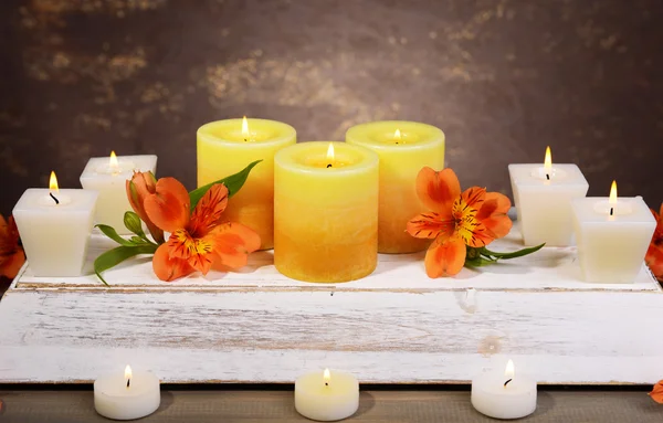 Hermosas velas con flores en la mesa sobre fondo marrón —  Fotos de Stock