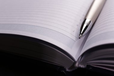 pen op geopend boek over zwarte tabel, close-up
