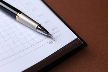 kahverengi masa üzerinde açık kitap üzerine kalem