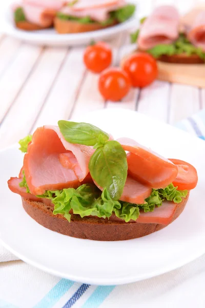 Läcker smörgås med sallad och skinka på tallriken på bordet närbild — Stockfoto