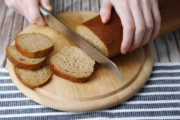 Female hands cutting bread on wooden board, close-up — Stock Photo, Image