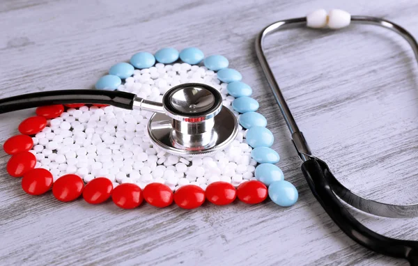 Heart of pills and stethoscope on wooden background — Stock Photo, Image