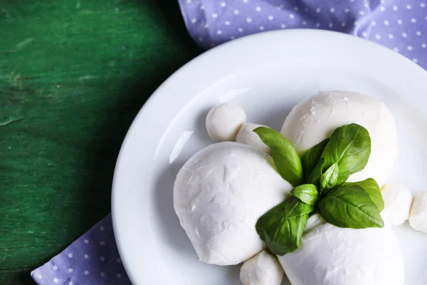 Smakelijke mozzarella kaas met basilicum op plaat op houten achtergrond — Stockfoto