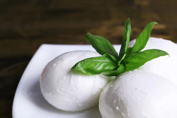 Schmackhafter Mozzarella-Käse mit Basilikum auf Teller auf Holzgrund — Stockfoto