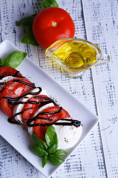 Ensalada Caprese con queso mozarella, tomates y albahaca en plato, sobre fondo de mesa de madera — Foto de Stock