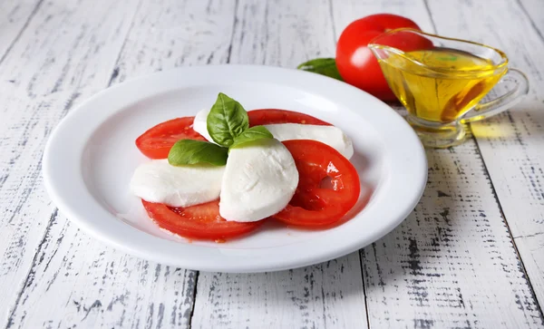 Caprese salad with mozarella cheese, tomatoes and basil on plate, on wooden table background — Stock Photo, Image