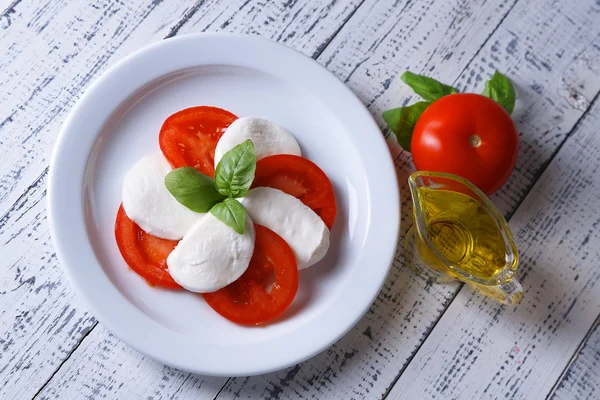 Caprese salad with mozarella cheese, tomatoes and basil on plate, on wooden table background — Stock Photo, Image