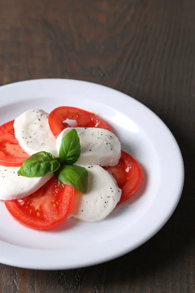 Caprese-Salat mit Mozarella, Tomaten und Basilikum auf Tellern, auf Holztischhintergrund — Stockfoto