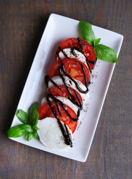 Caprese-Salat mit Mozarella, Tomaten und Basilikum auf Teller, auf Holztischhintergrund — Stockfoto