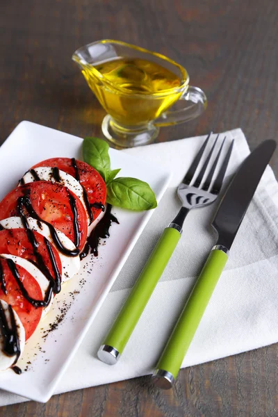 Ensalada Caprese con queso mozarella, tomates y albahaca en plato, sobre fondo de mesa de madera — Foto de Stock