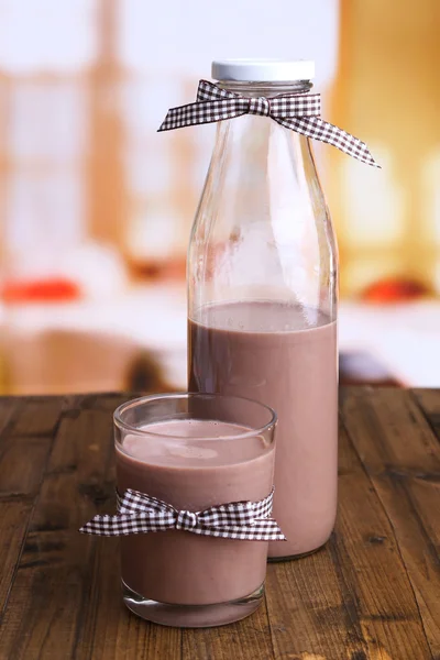 Chokolademælk i flaske og glas, på træbord, på lys baggrund - Stock-foto