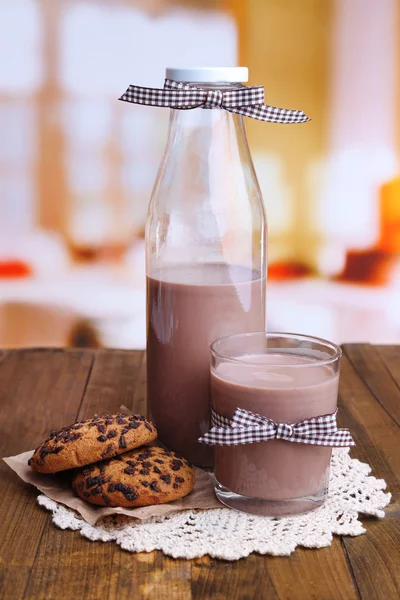 Chocolate milk in bottle and glass, on wooden table, on bright background — Stock Photo, Image