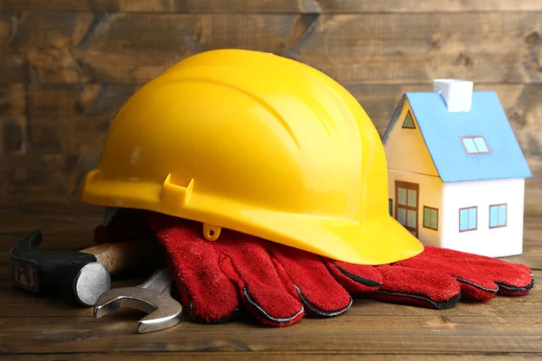 Composition with safety helmet, leather gloves, tools and decorative house on wooden background — Stock Photo, Image