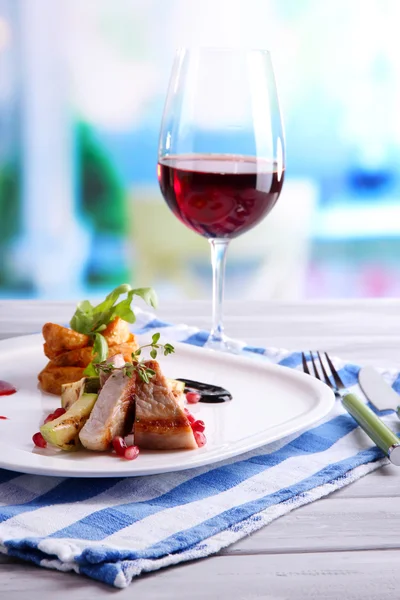 Grilled meat  with fried potato, marrow pieces and pomegranate seeds on plate, on wooden table, on bright background — Stock Photo, Image