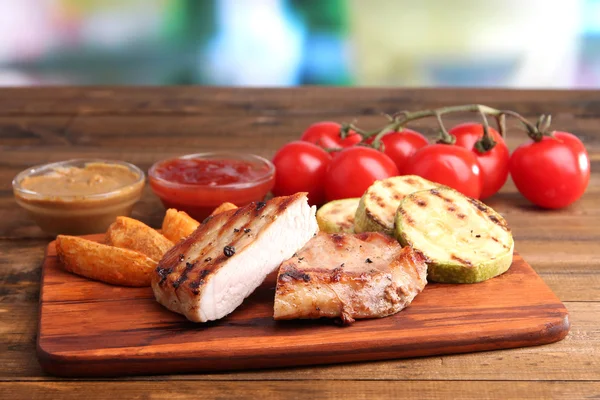 Bistecca alla griglia, verdure alla griglia e pezzi di patate fritte su tavola di legno sullo sfondo del tavolo — Foto Stock