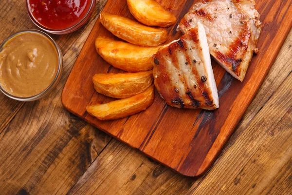 Gegrilltes Steak, gegrilltes Gemüse und gebratene Kartoffelstücke auf Holzbrett auf Tischhintergrund — Stockfoto