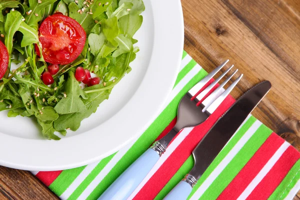 Зелений салат з руколи, помідорів і кунжуту на тарілці, на дерев'яному фоні — стокове фото