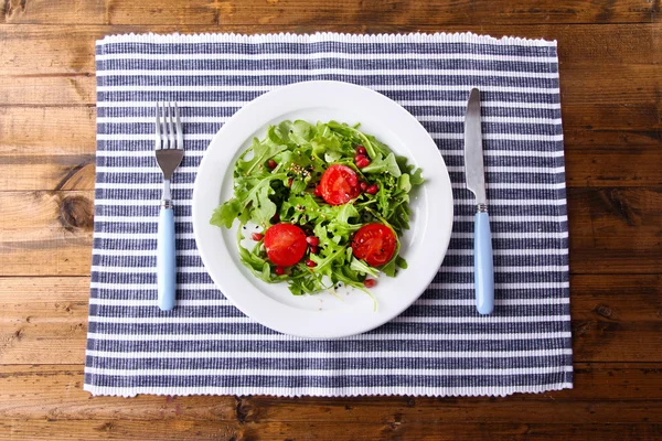 Grüner Salat mit Rucola, Tomaten und Sesam auf Teller, auf Holzgrund — Stockfoto