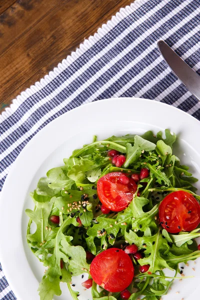 Salada verde feita com arugula, tomates e gergelim na placa, no fundo de madeira — Fotografia de Stock