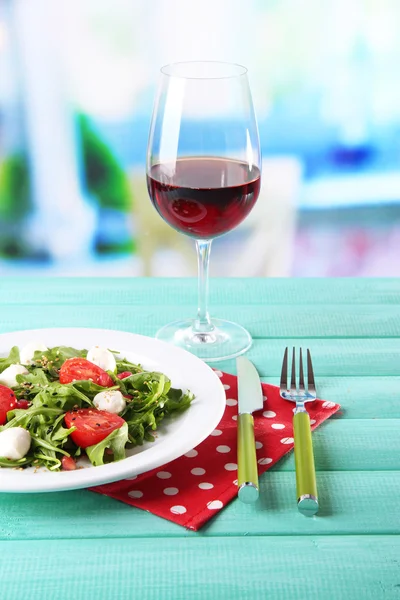 Green salad made with  arugula, tomatoes, cheese mozzarella balls and sesame  on plate, on table, on bright background — Stock Photo, Image