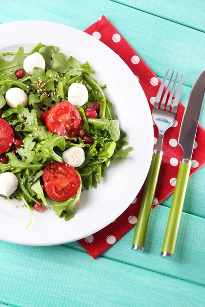Groene salade gemaakt met rucola, tomaten, kaas mozzarella ballen en sesam op plaat, op een houten achtergrond kleur — Stockfoto