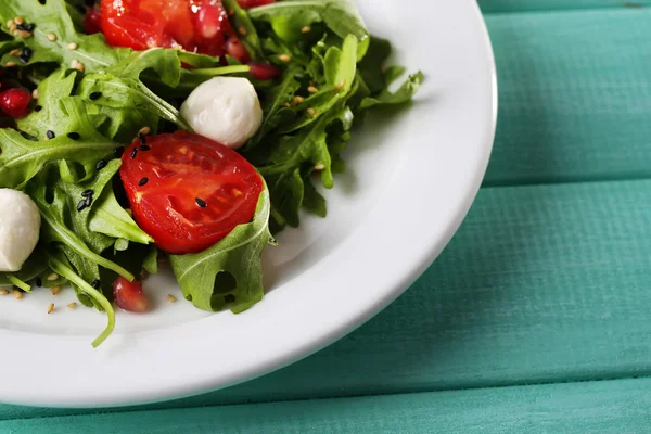 Salada verde feita com arugula, tomates, bolas de mussarela de queijo e gergelim na placa, na cor de fundo de madeira — Fotografia de Stock