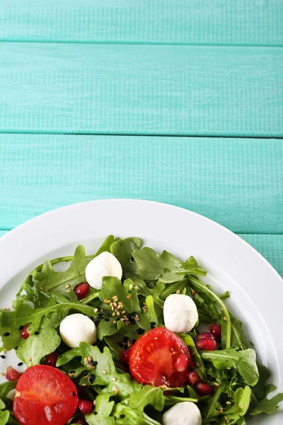 Grön sallad med rucola, tomater, ost mozzarella bollar och sesam på plattan, färg trä bakgrund — Stockfoto