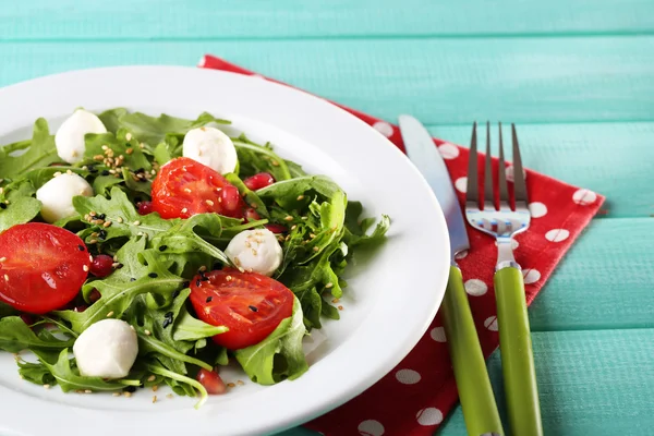 Ensalada verde hecha con rúcula, tomates, bolas de queso mozzarella y sésamo en plato, sobre fondo de madera de color —  Fotos de Stock