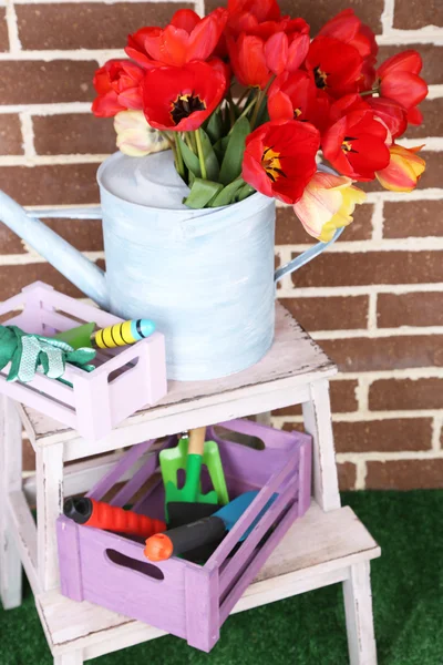 Komposition aus bunten Tulpen in Gießkanne und Gartengeräten auf hellem Hintergrund — Stockfoto