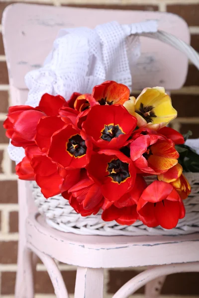 Kytice barevné tulipány v proutěném koši, na židli, na domácí interiér pozadí — Stock fotografie