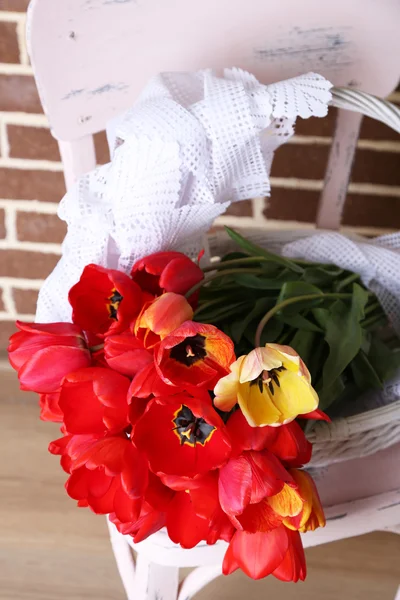 Bouquet of colorful tulips in wicker basket, on chair, on home interior background — Stock Photo, Image