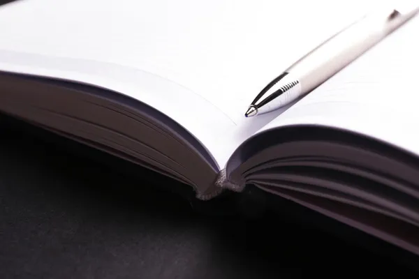 Pen on opened book on black table, close up — Stock Photo, Image