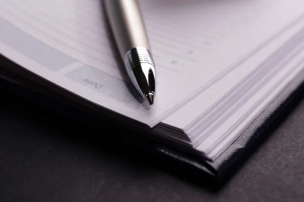 Pen on opened book on black table, close up — Stock Photo, Image