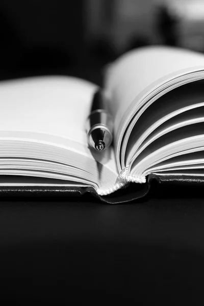 Caneta sobre livro aberto na mesa preta, close-up — Fotografia de Stock