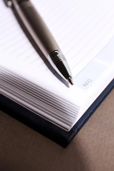 Stift auf aufgeschlagenem Buch auf braunem Tisch, Nahaufnahme — Stockfoto