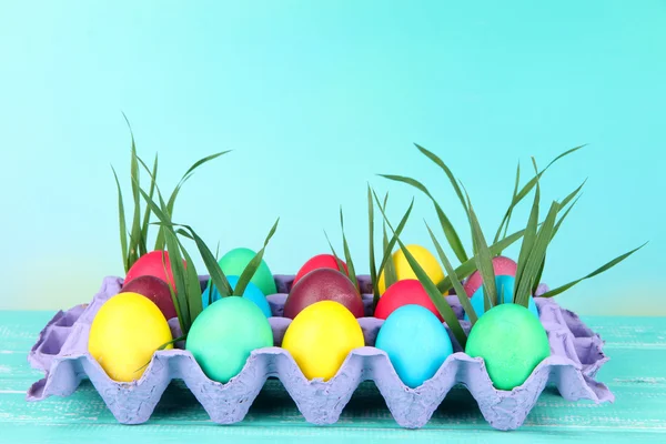 Colorful Easter eggs with grass in tray on table on bright background — Stock Photo, Image