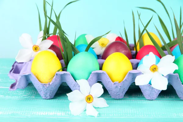 Барвисті великодні яйця з травою і квітами в лотку на столі на яскравому фоні — стокове фото
