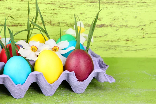 Huevos de Pascua coloridos con hierba y flores en bandeja sobre mesa sobre fondo de madera — Foto de Stock