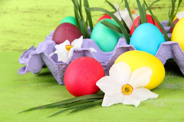 Colorful Easter eggs with grass and flowers in tray on table on wooden background — Stock Photo, Image