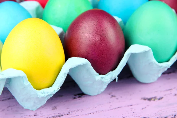 Barevné velikonoční vejce v zásobníku na dřevěné pozadí — Stock fotografie