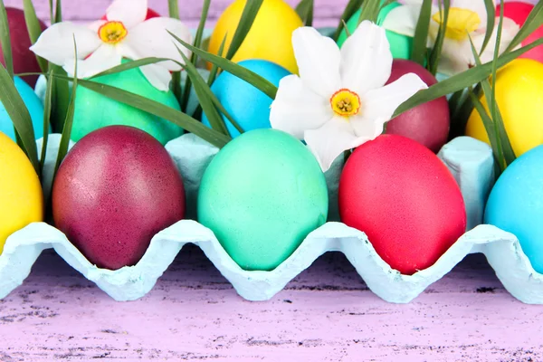 Colorful Easter eggs with grass and flowers in tray on wooden background — Stock Photo, Image