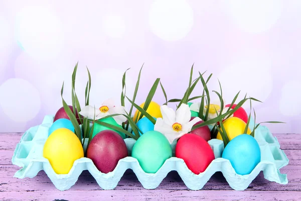 Œufs de Pâques colorés avec herbe et fleurs dans un plateau sur la table sur fond lumineux — Photo