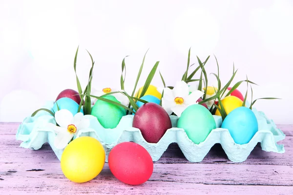 Huevos de Pascua coloridos con hierba y flores en bandeja sobre la mesa sobre fondo brillante — Foto de Stock
