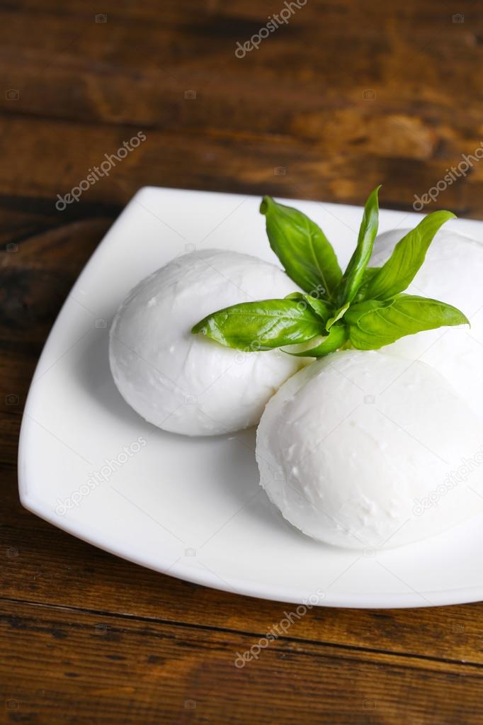 Tasty mozzarella cheese with basil on plate  on wooden background