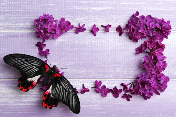 Schöne lila Blumen und Schmetterling auf hölzernem Hintergrund — Stockfoto