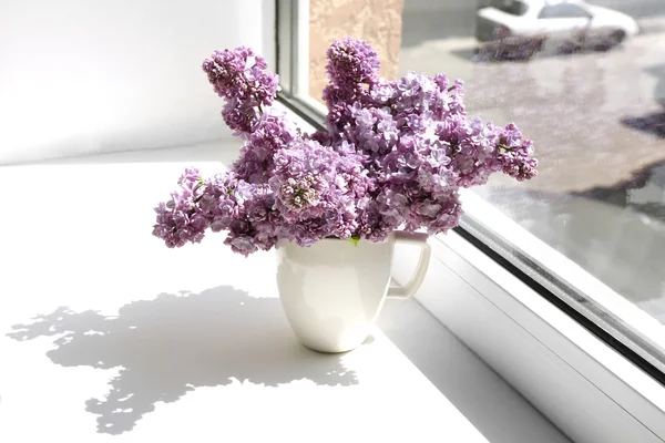 Beautiful lilac flowers on windowsill — Stock Photo, Image